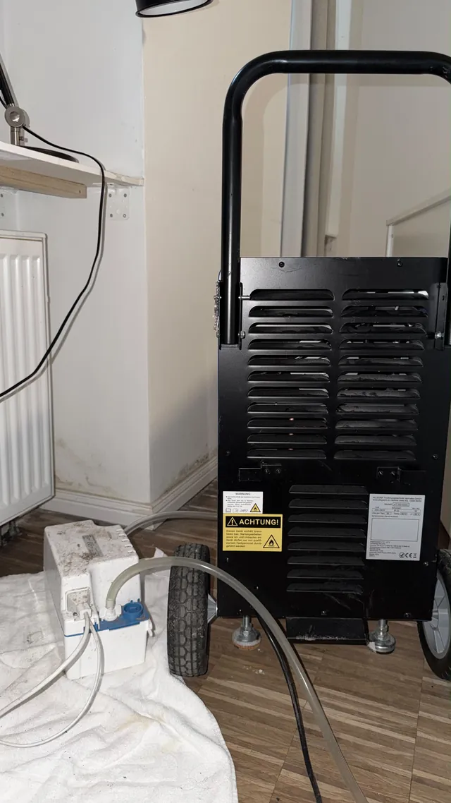 Trockner mit Kondensatpumpe neben einem feuchtegeschädigten Wandanschluss