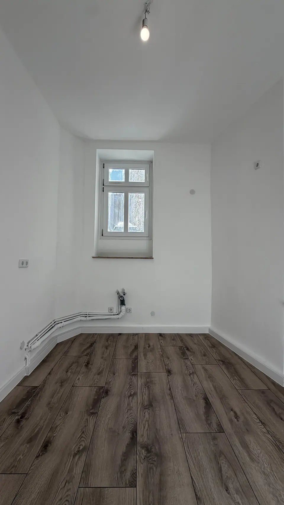 Küchenraum nach der Sanierung mit weißen Wandflächen, Boden in Holzoptik und sichtbaren Anschlüssen