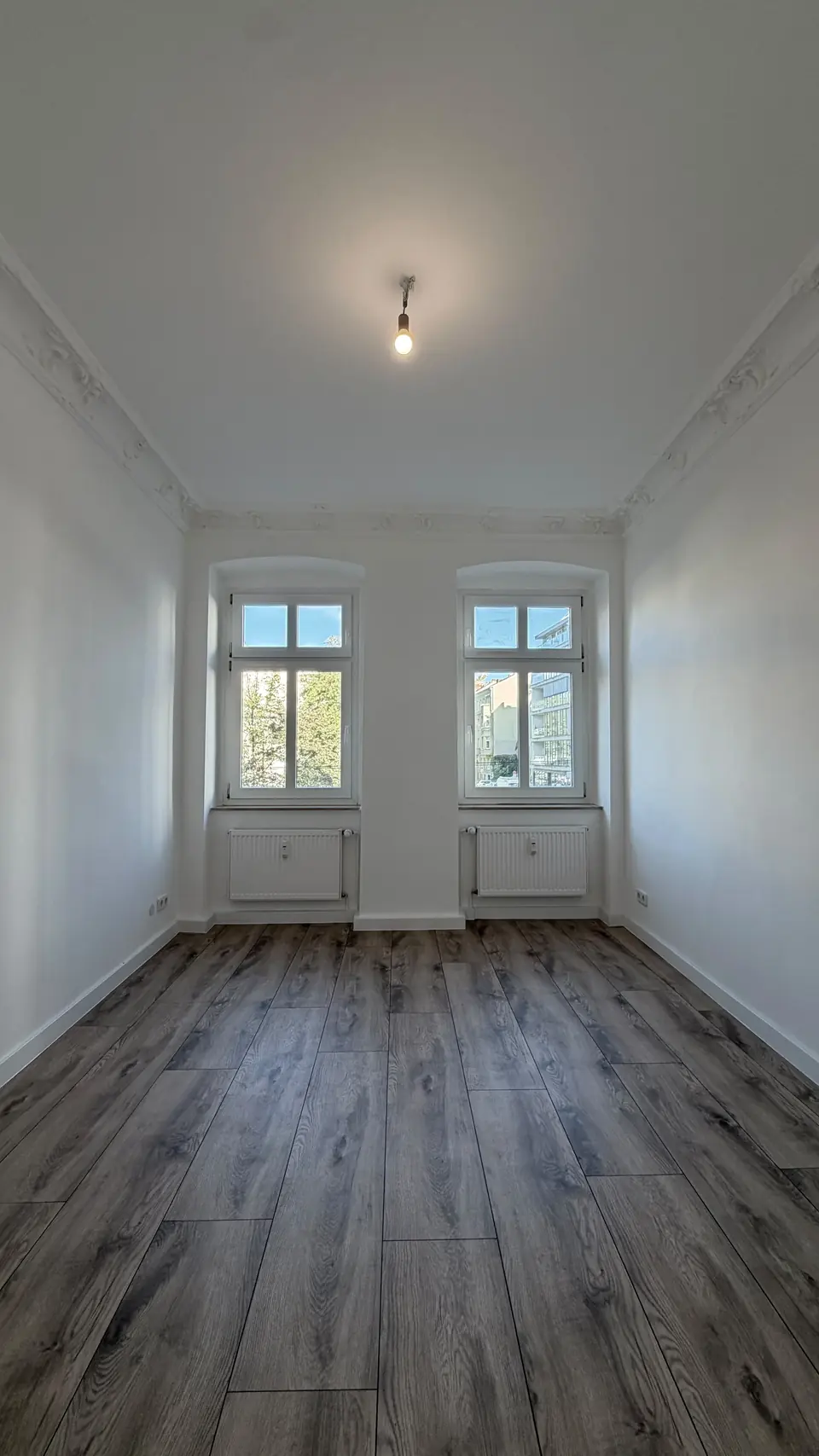 Wohnraum nach der Komplettsanierung in Berlin Mitte mit weißen Wänden und Boden in Holzoptik