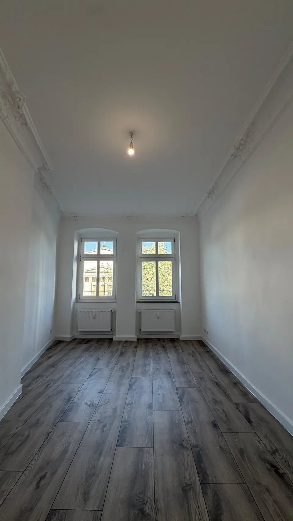 Weiterer Altbauraum nach der Sanierung mit weißen Wänden, Stuck und Boden in Holzoptik